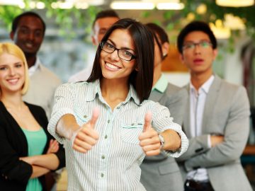 Happy businesswoman standing with thumbs up in front her colleagues